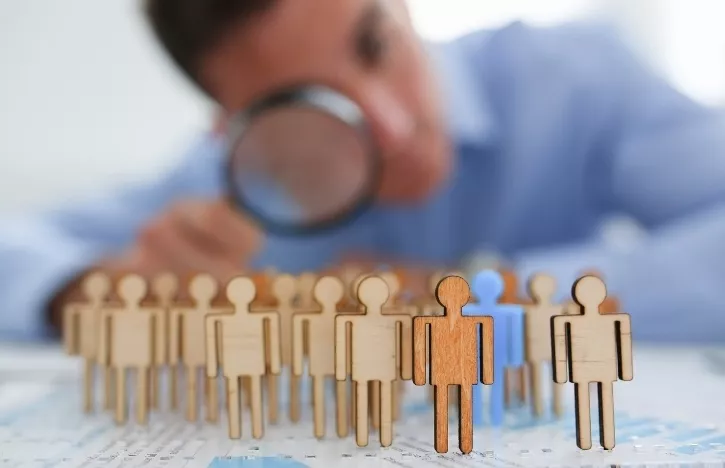 man looking through magnifying glass at wooden people - Surveillance Evasion course concept at PWA.edu