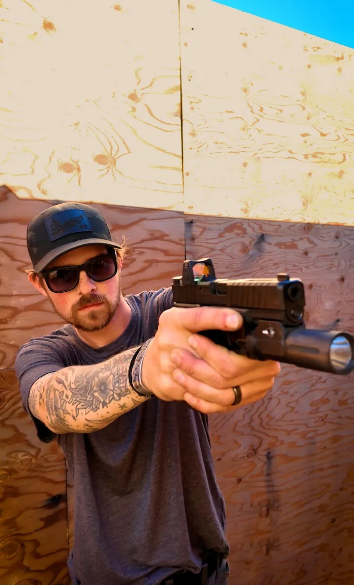 Man in a cap aiming a handgun with a two-handed grip during firearms training
